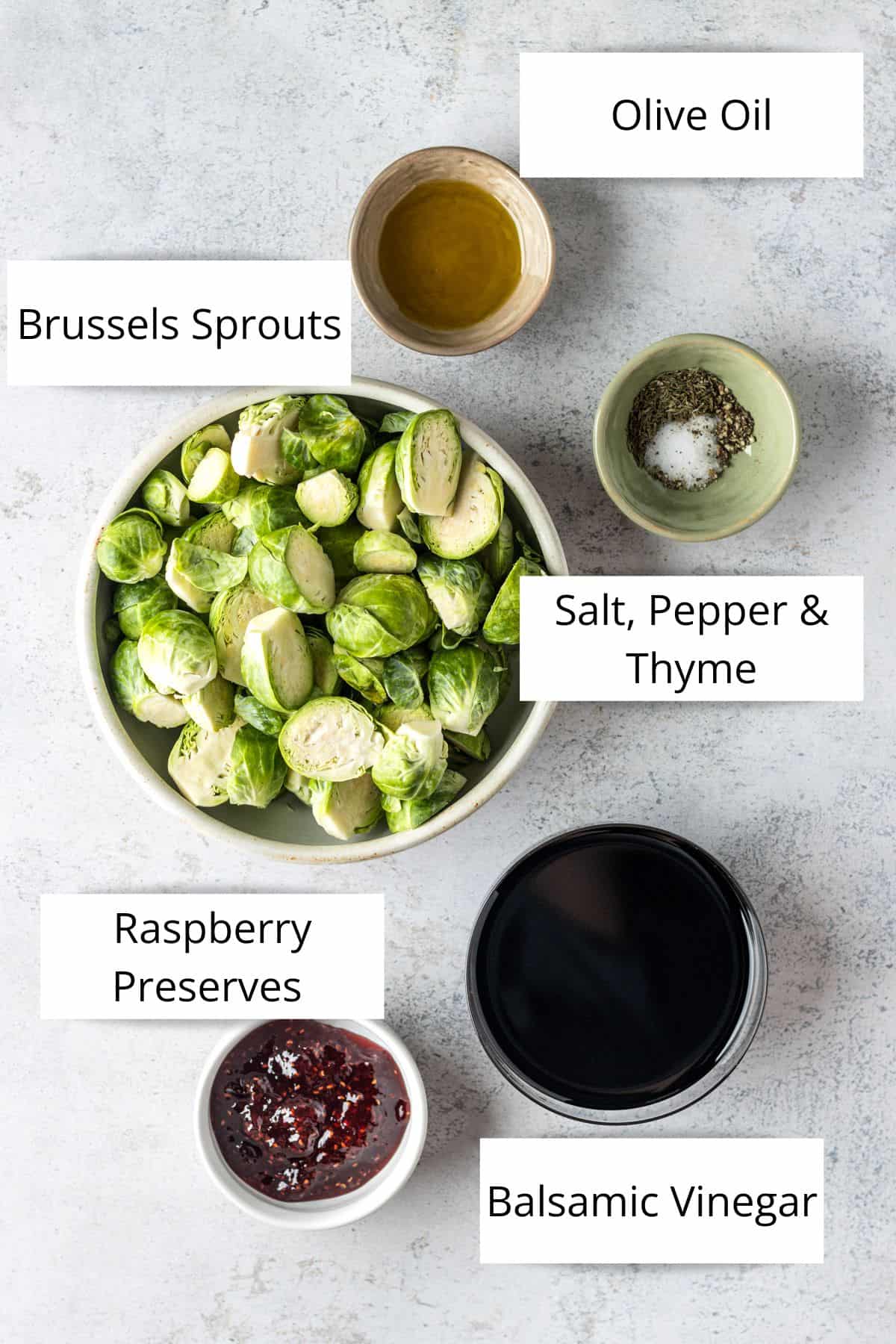 A while bowl with halved Brussels sprouts, a pinch bowl of olive oil, a pinch bowl of spices, a small while bowl with raspberry preserves and a clear bowl with balsamic vinegar.