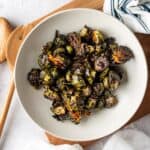 A large white bowl on a cutting board filled with oven roasted Brussels sprouts with balsamic glaze.