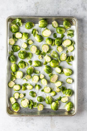 A baking sheet with parchment paper with halved Brussels sprouts.