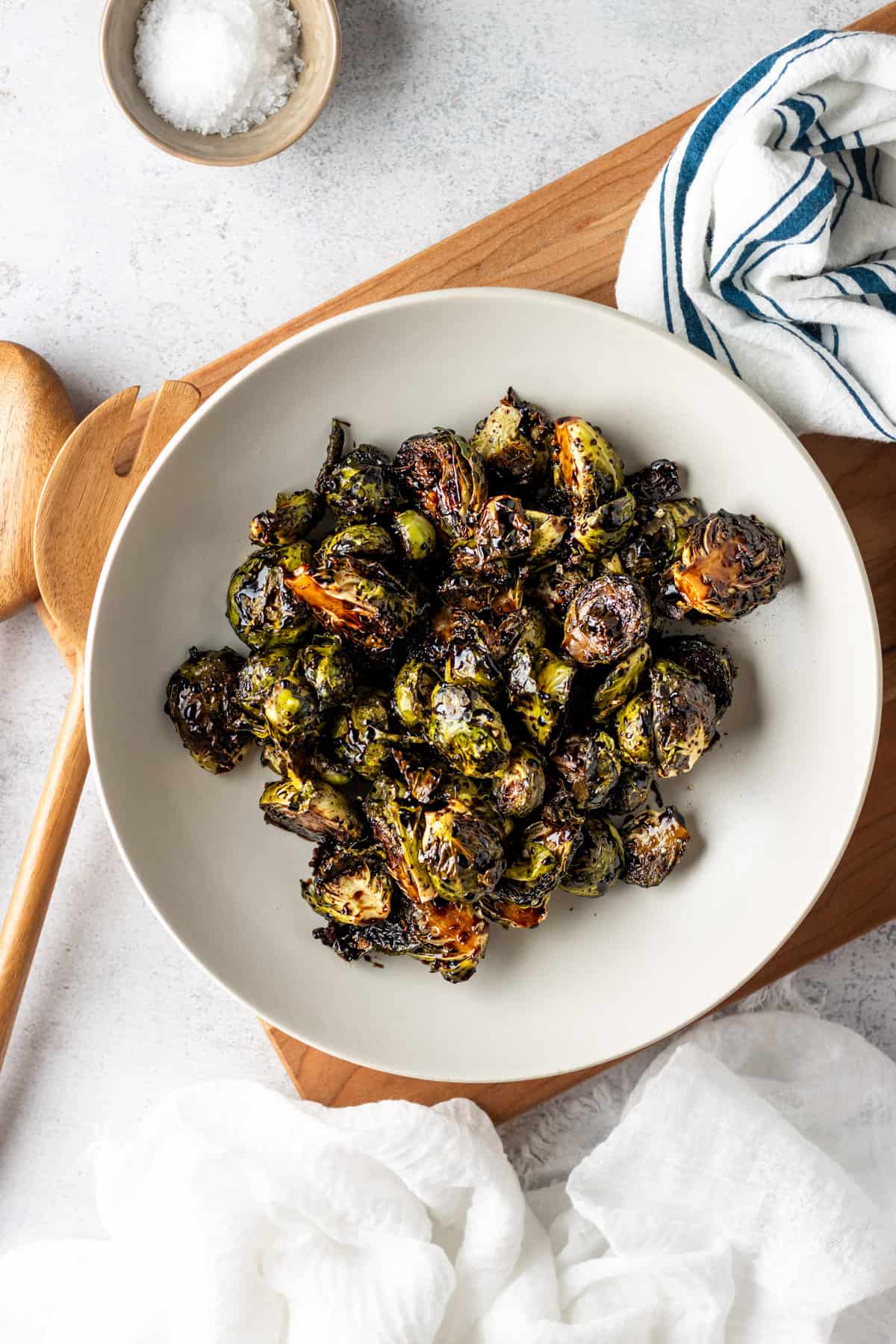 Brussels sprouts in a while bowl on a wooden cutting board tossed with raspberry balsamic glaze.