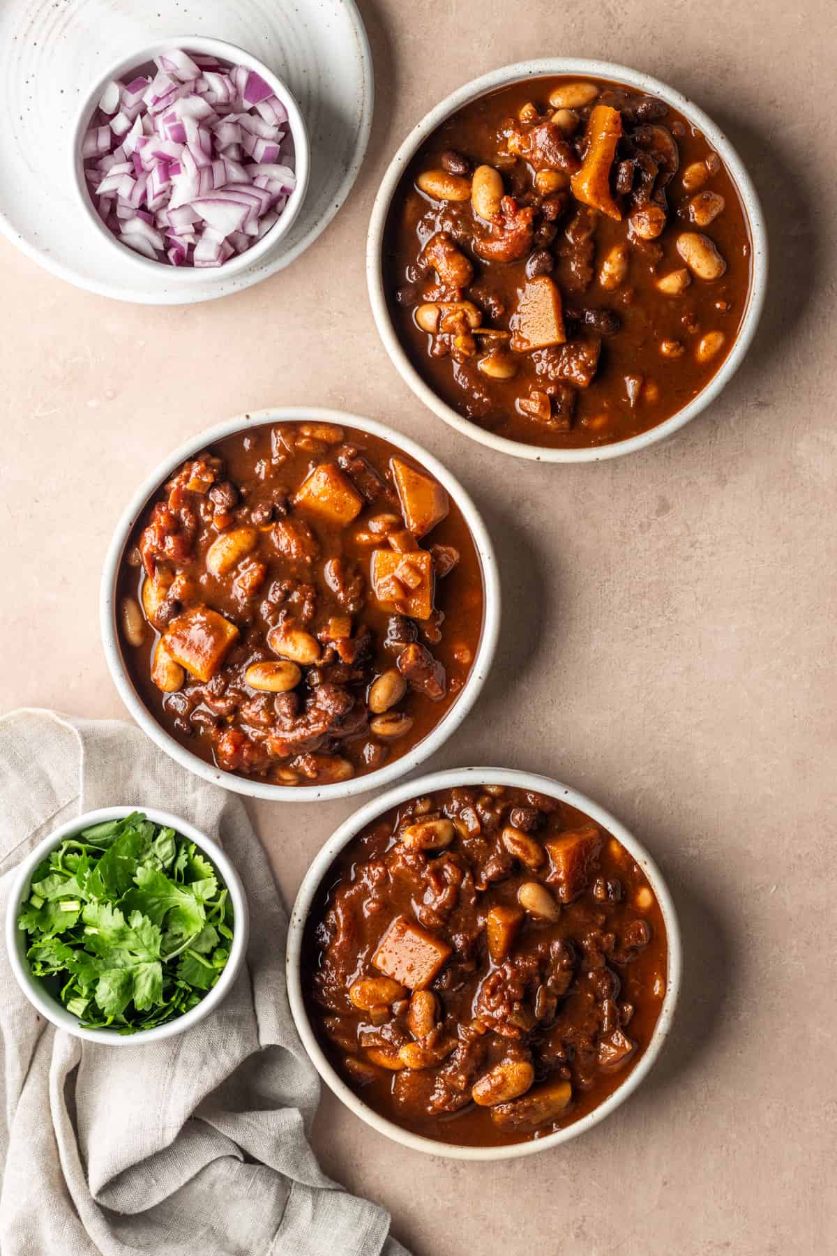3 Bowls of vegetarian beer chili with pinch bowls of cilantro and red onions.