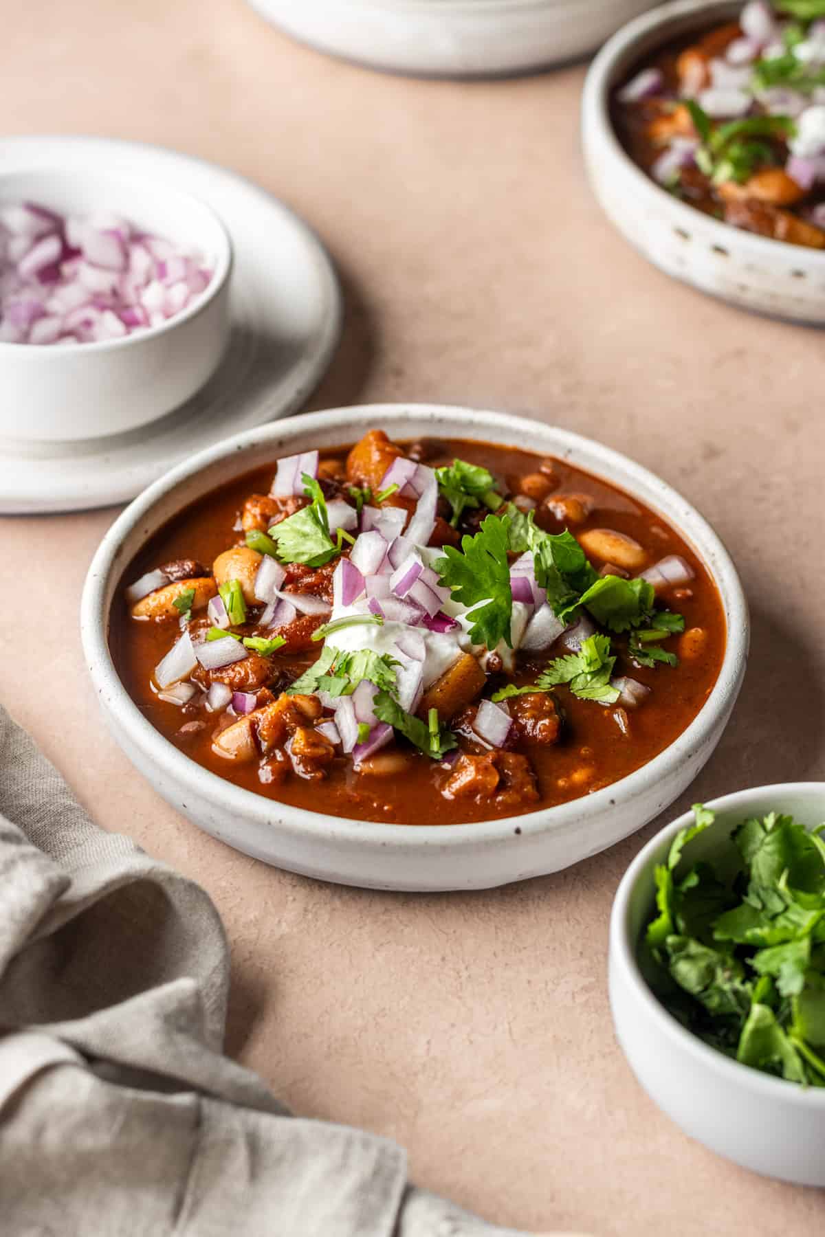 A white bowl of butternut squash beer chili garnished with yogurt, diced red onion and cilantro.