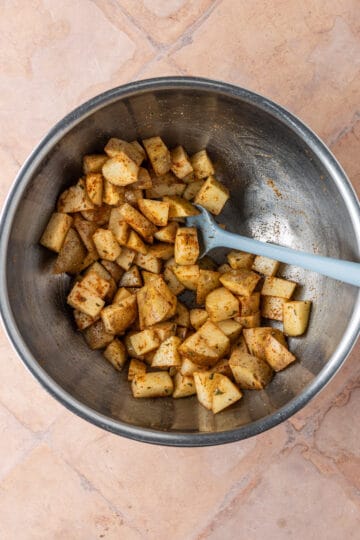 Overhead of cubed white potatoes in a mixing bowl mixed with spices.
