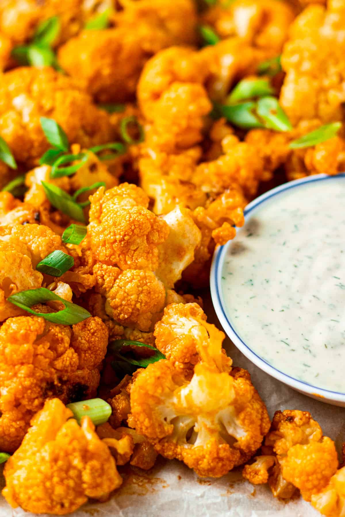 Close up of roasted buffalo cauliflower garnished with sliced green onions and a bowl of ranch dipping sauce.