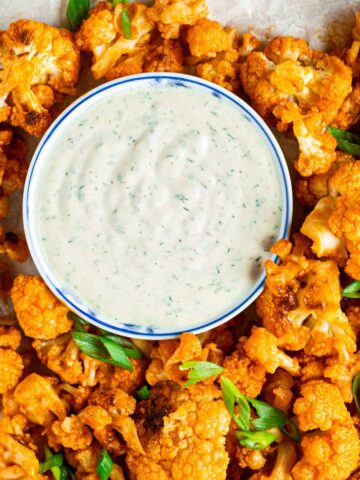 Overhead view of roasted cauliflower wings garnished with green onions with a small bowl of ranch.