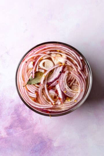 Overhead of sliced red onions and spices in a pyrex bowl covered in brine for picking.