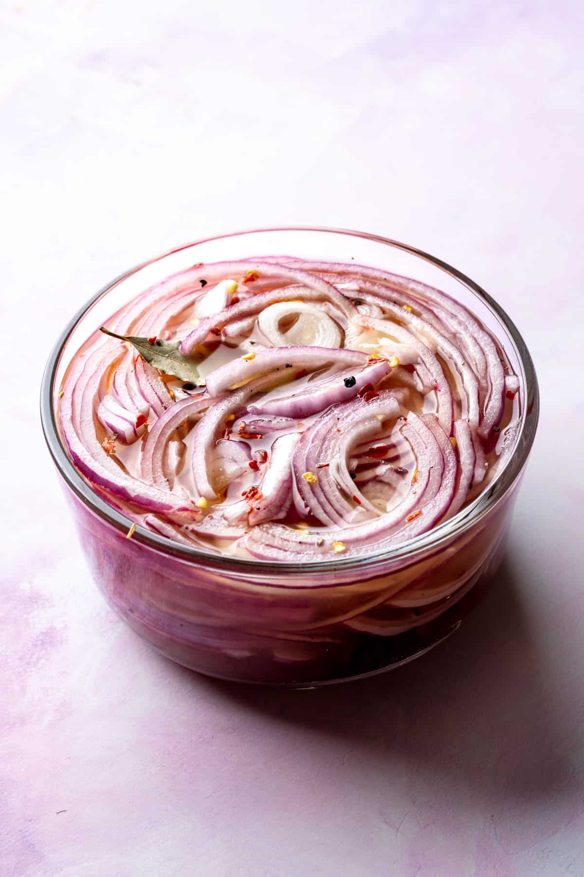 A glass bowl of sliced pickled red onions with spices.