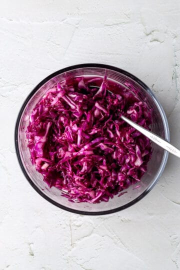 A glass bowl with shredded red cabbage and a spoon.