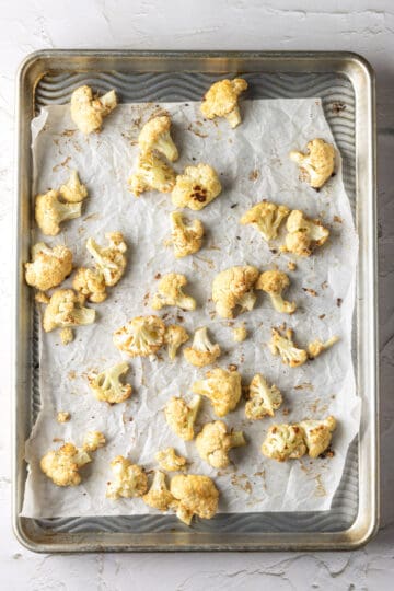 Overhead of a baking sheet lined with parchment paper and roasted cauliflower.