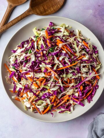 Overhead view of a colorful cabbage and carrot salad in a white bowl with a wooden utensils.