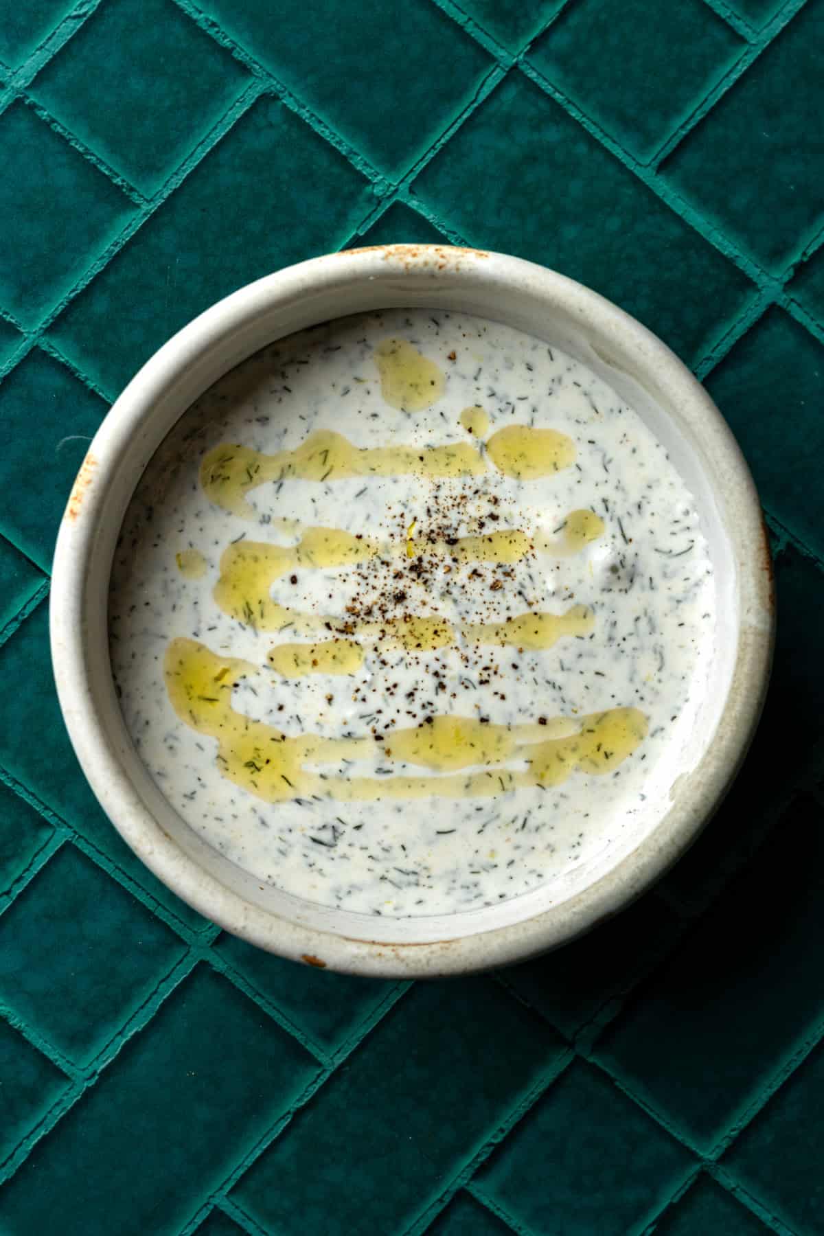 A white bowl of dill vegetable dip with a drizzle of olive oil.