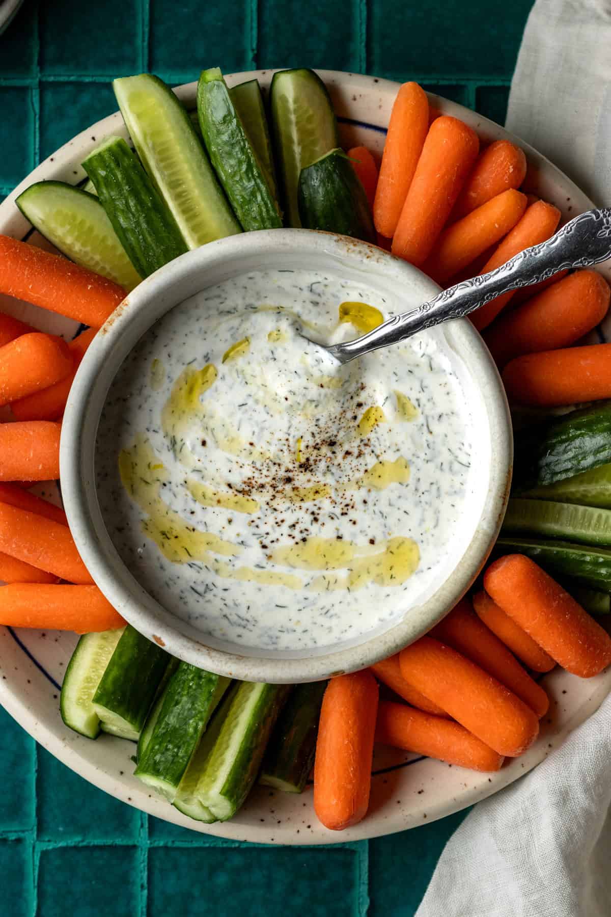 A platter of sliced cucumbers and carrots with a bowl of dill vegetable dip.