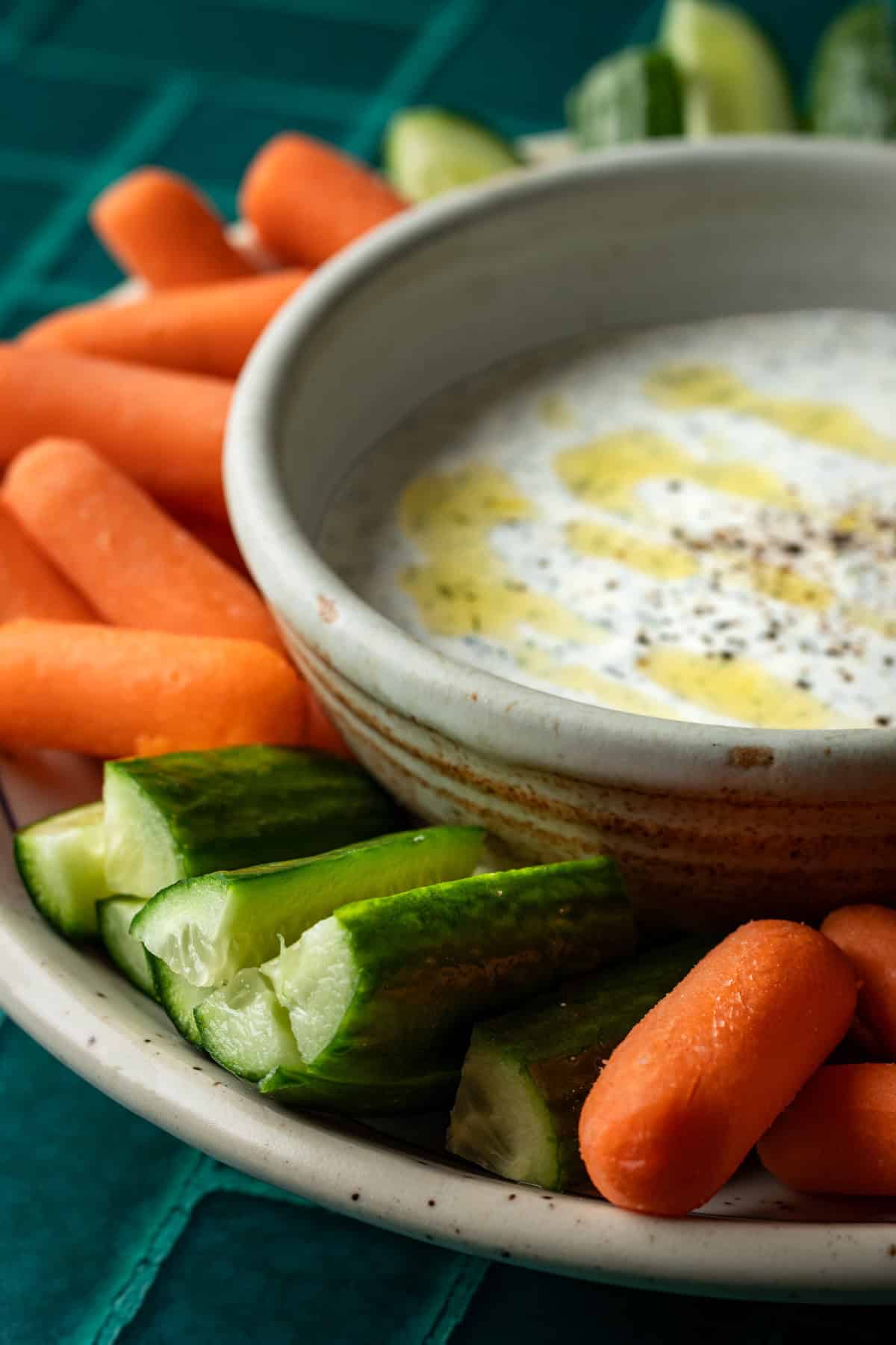 A close up of carrots and cucumbers with a bowl of greek yogurt dill dip.