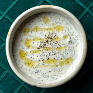 A bowl of greek yogurt dill dip with a drizzle of olive oil.