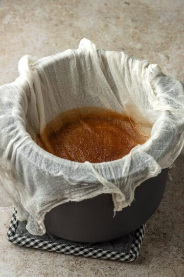 A cheesecloth over a large pot straining broth.