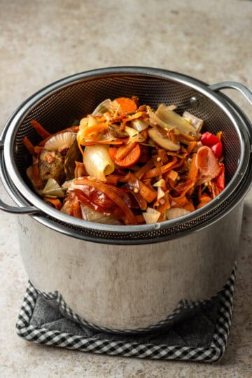 A strainer over a large pot with vegetable scraps.