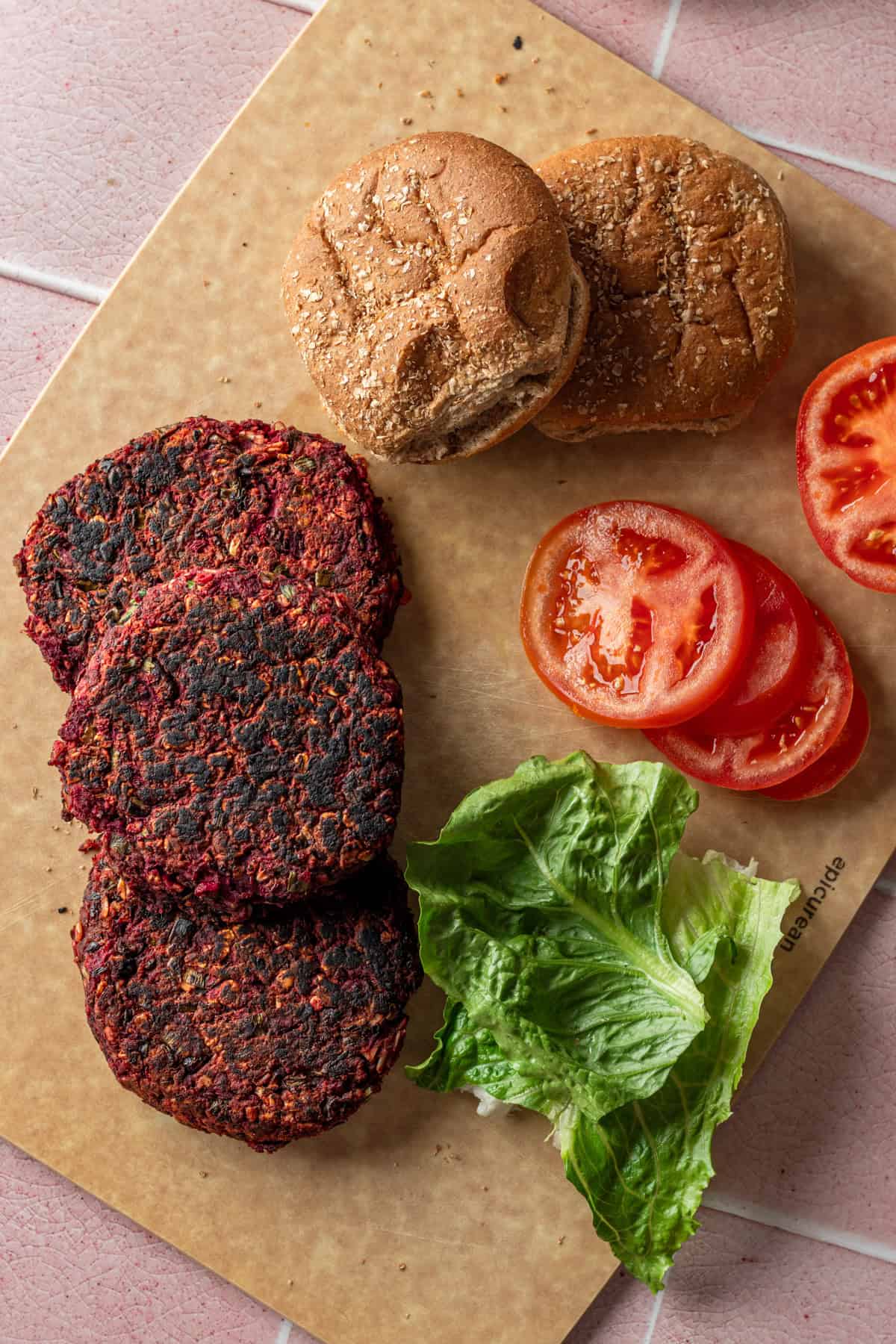 A cutting board with veggie burgers, buns, lettuce and tomatoes.