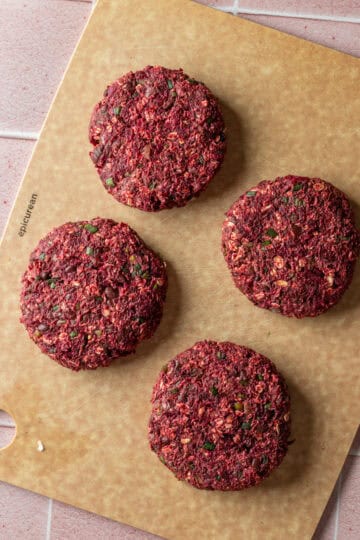 Four black bean beet burger patties on a cutting board.