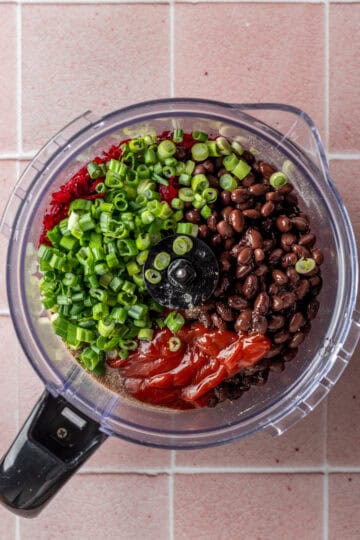 A food processor with black beans, green onions, beets and ketchup.