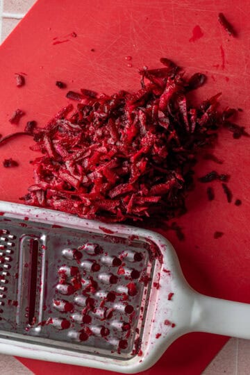 Grated beets on a red cutting board.