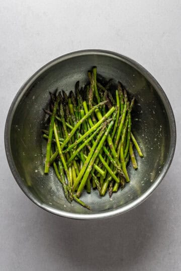 A large mixing bowl with asparagus tossed in oil and garlic.