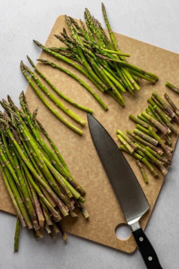 A cutting board with asparagus and their ends being cut off.