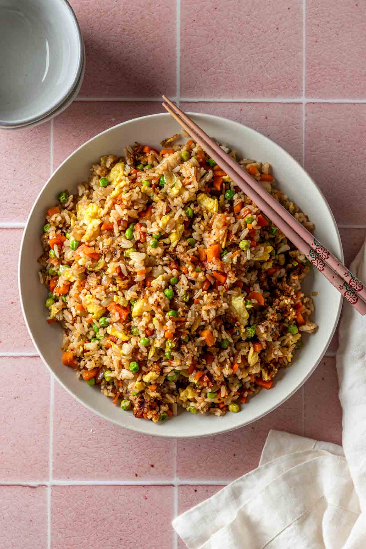 Overhead of a bowl of vegetable fried rice with pink chopsticks on the side of the bowl.