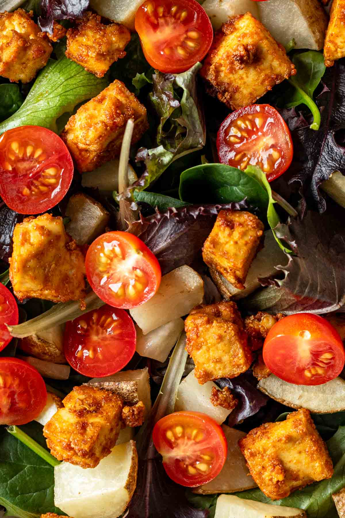 Close up of salad with mixed greens, tofu, potatoes and cherry tomatoes.