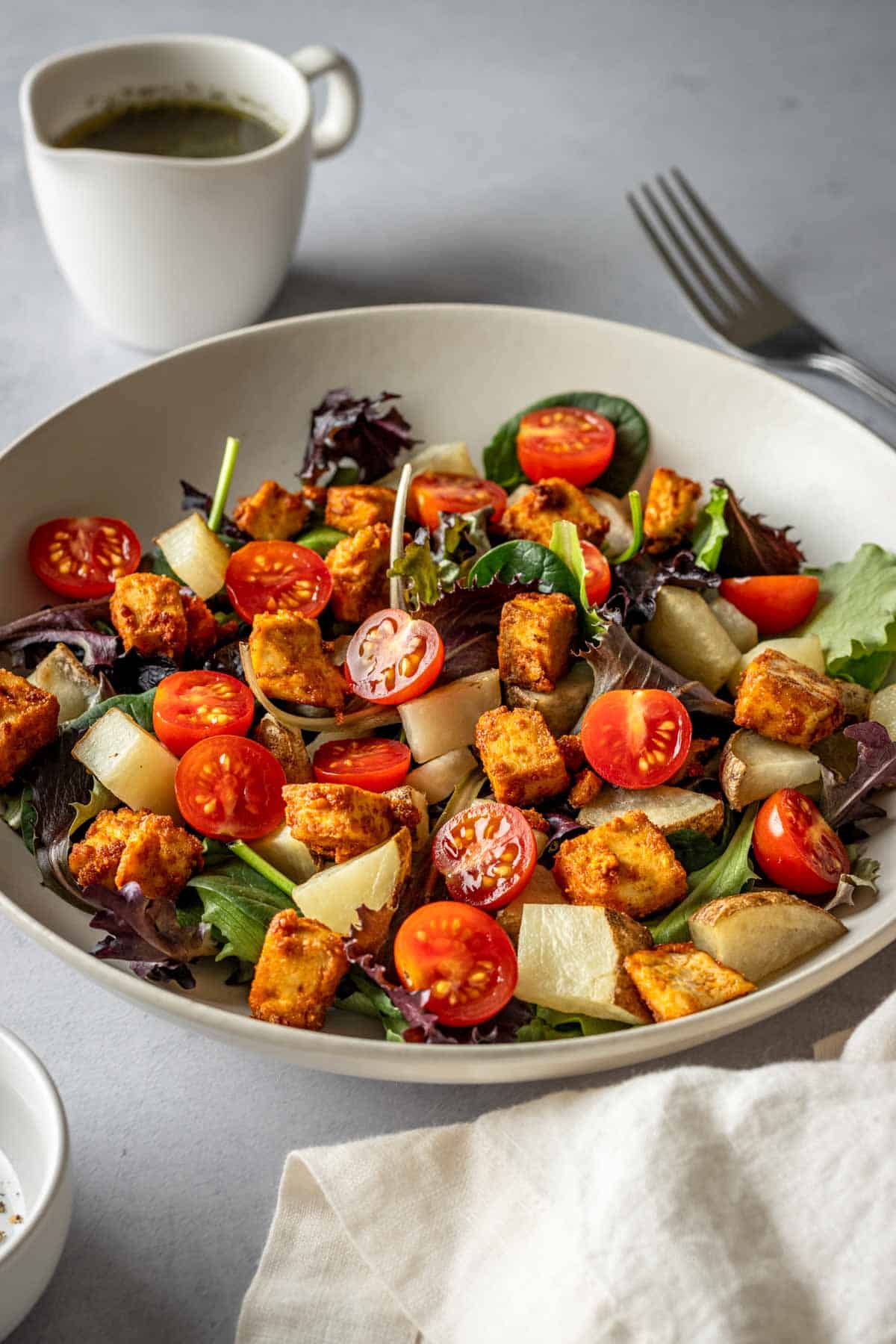 Mixed greens salad with tofu, potatoes and tomatoes with dressing on the side.