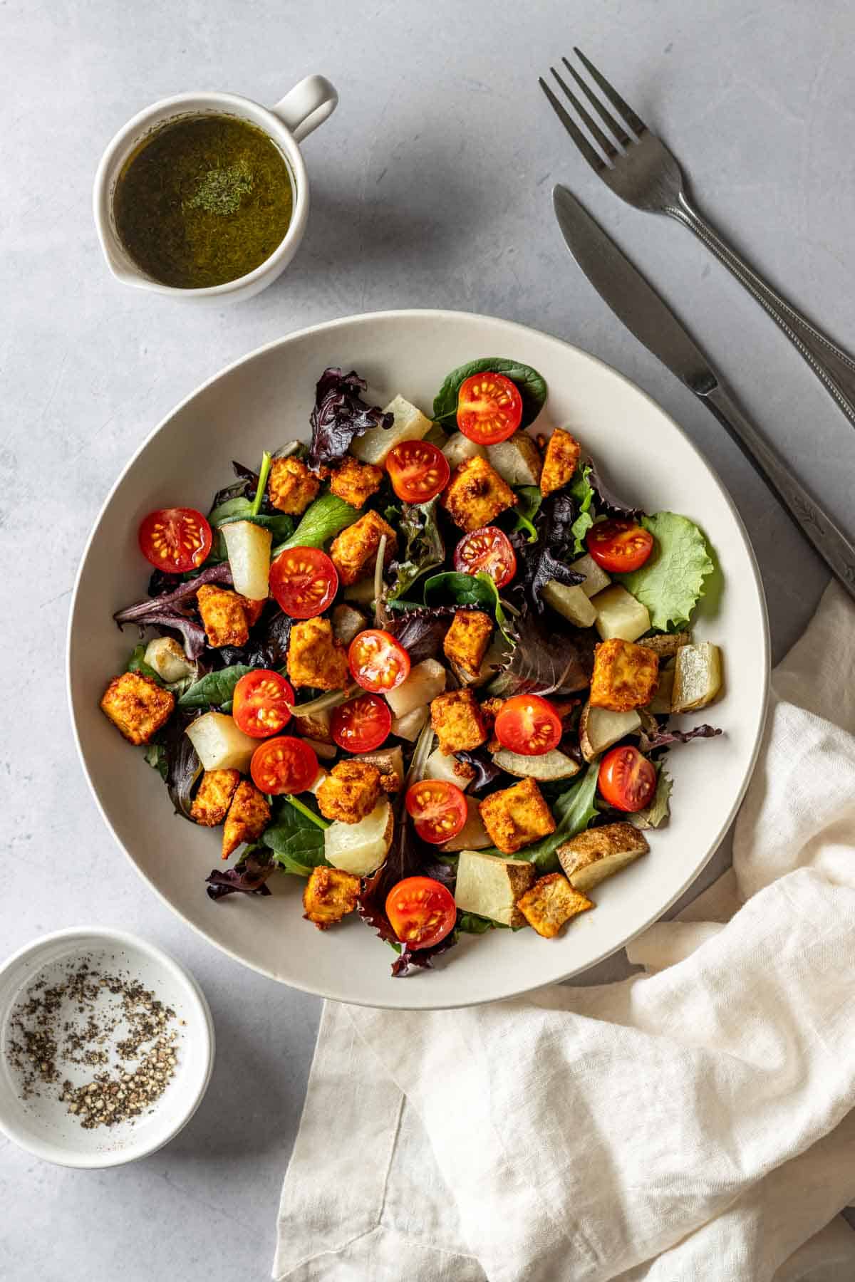 Vegan breakfast salad in a white bowl with dijon dressing on the side.