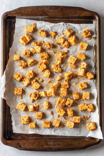 Cubed and seasoned tofu spread out on a baking sheet.