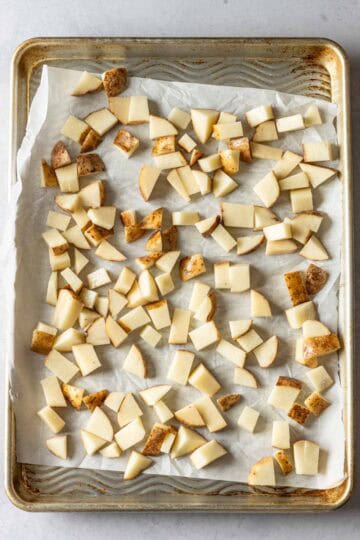 Cubed potatoes spread out on a baking sheet.