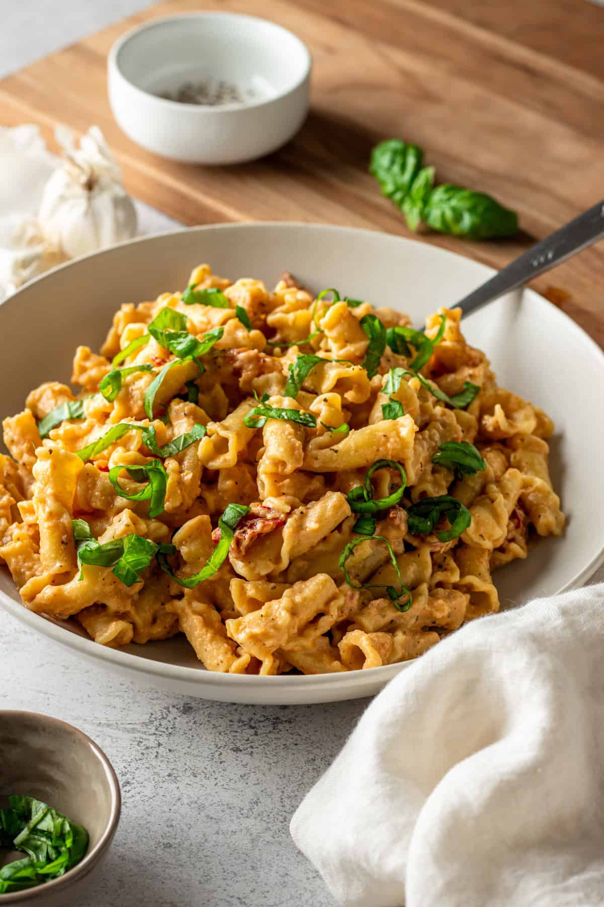 A bowl of pasta tossed in sun-dried tomato cauliflower sauce with basil.