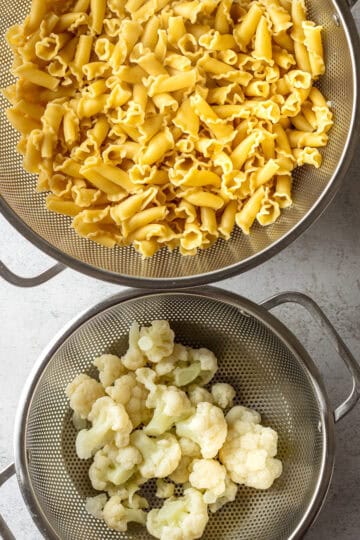 Two strainers with pasta and cauliflower.