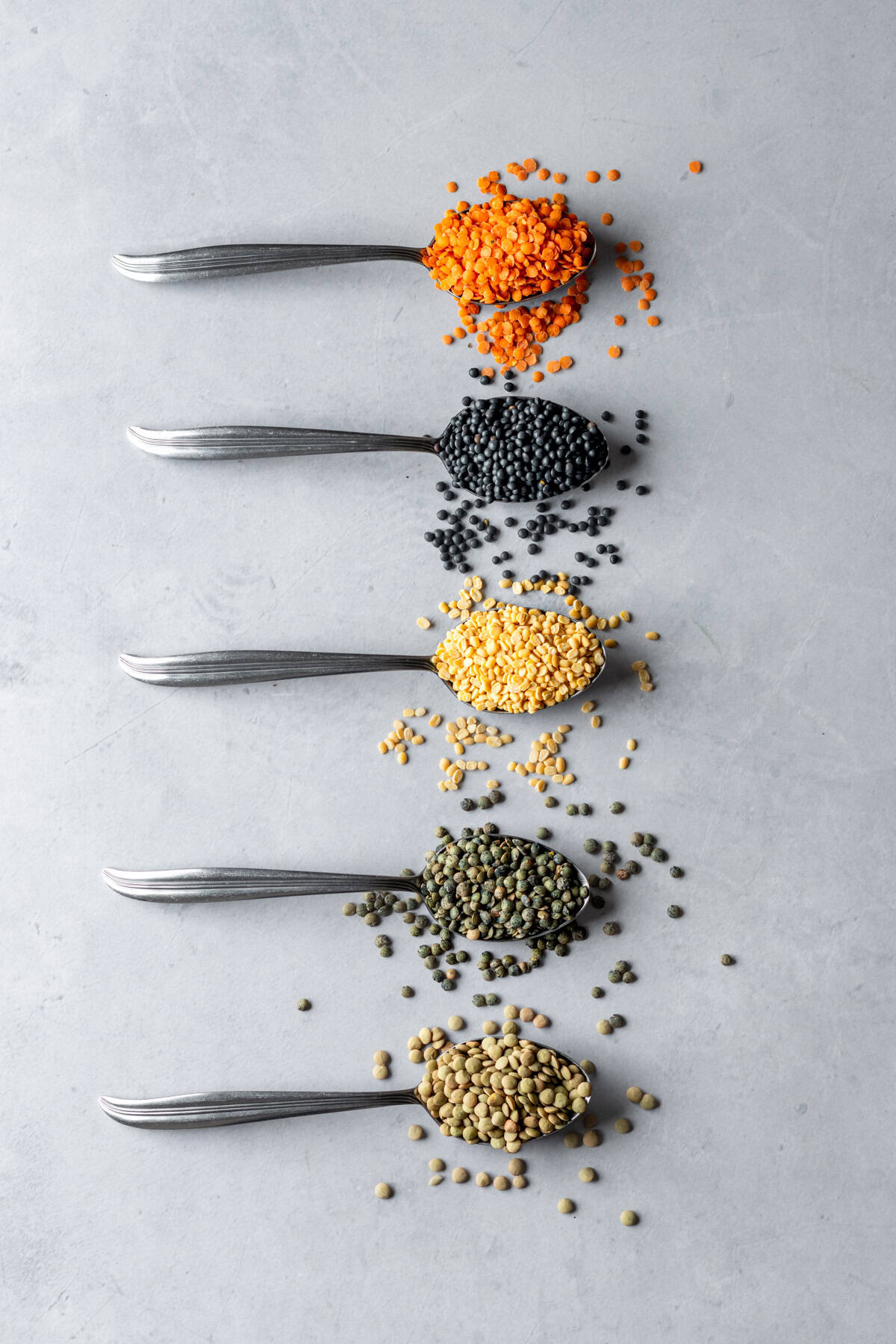 Five spoons filled with different lentil colors.