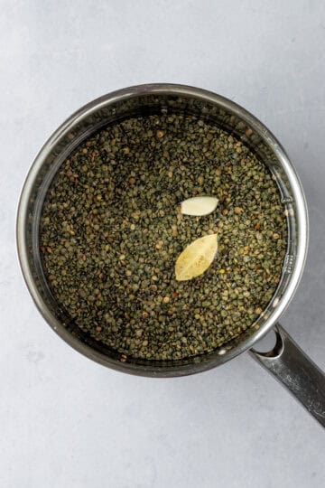 A saucepan with water, lentils, garlic and a bayleaf.