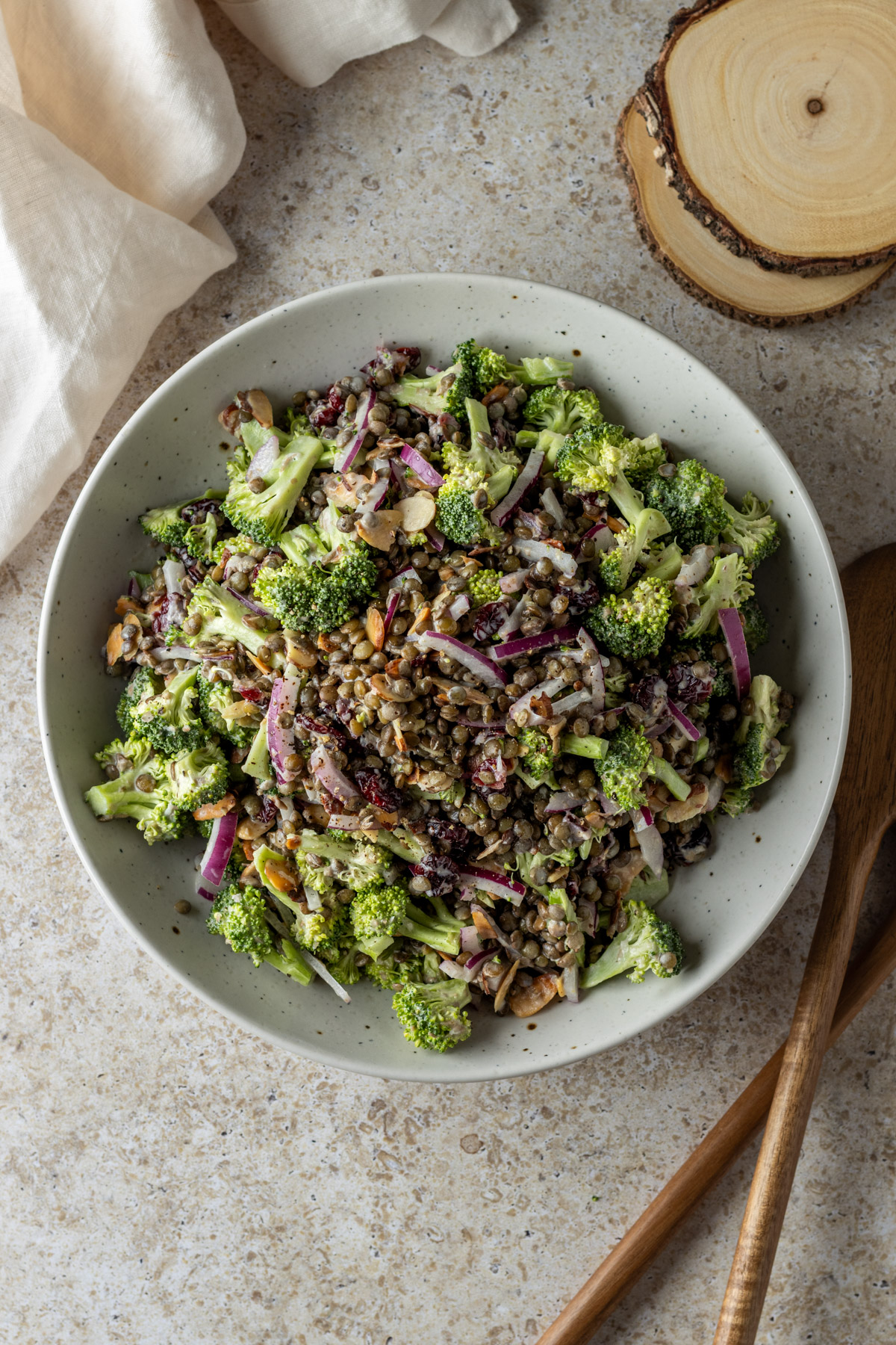 Broccoli lentil salad in a large bowl with wooden spoons on the side.