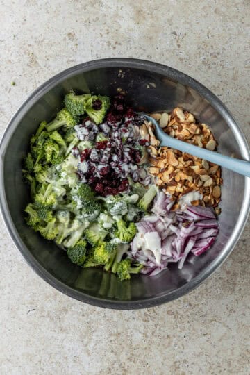 Mixing bowl with broccoli, dressing, red onion, almonds and dried cranberries.