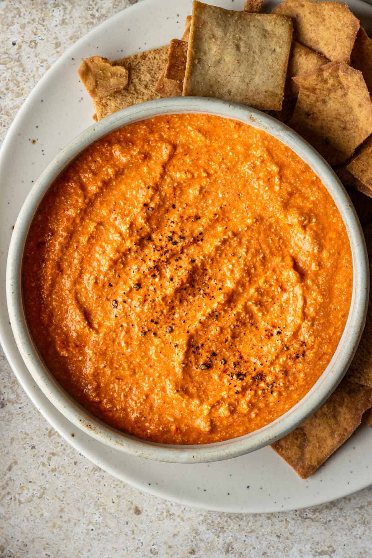 Roasted red pepper feta dip with pita chips on a serving platter.