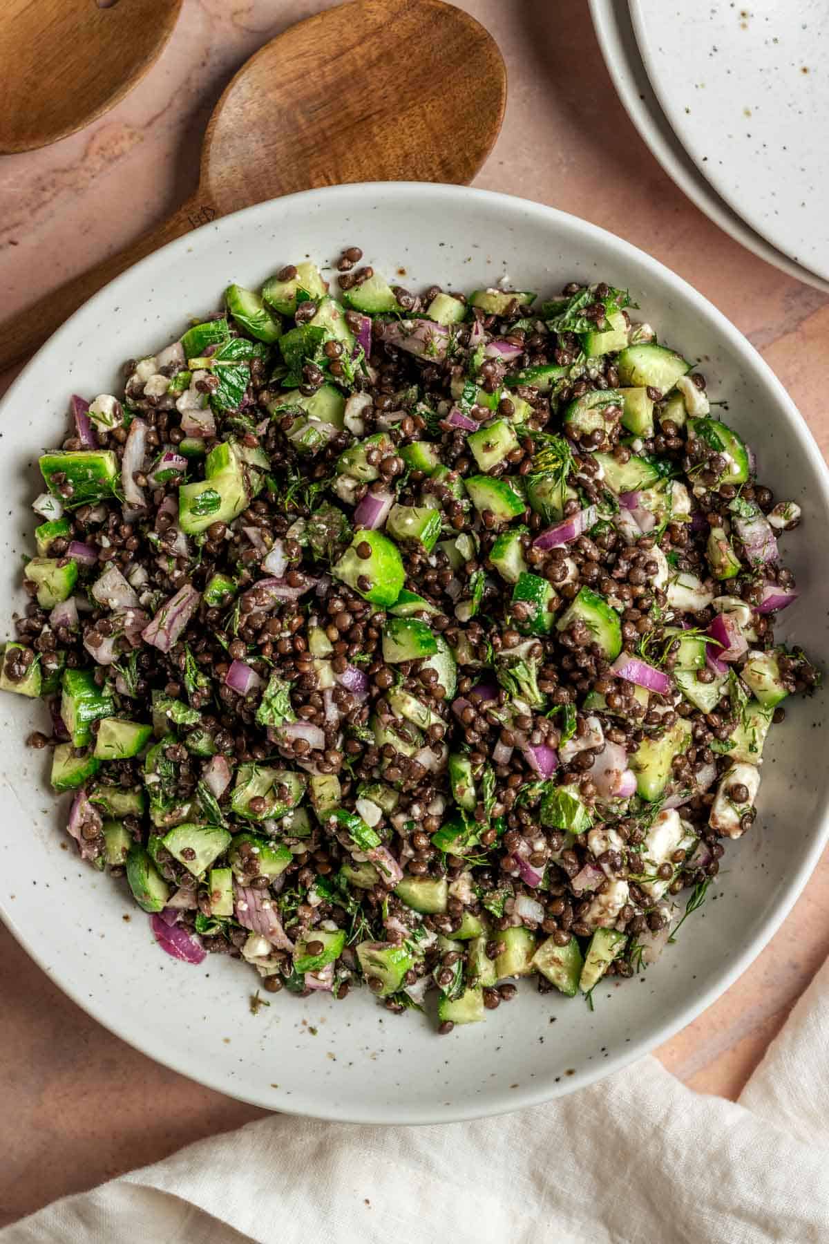 Lentil salad in a white bowl with wooden serving spoons.