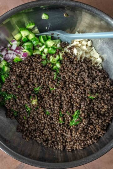 A large mixing bowl of lentils, diced vegetables and feta cheese.