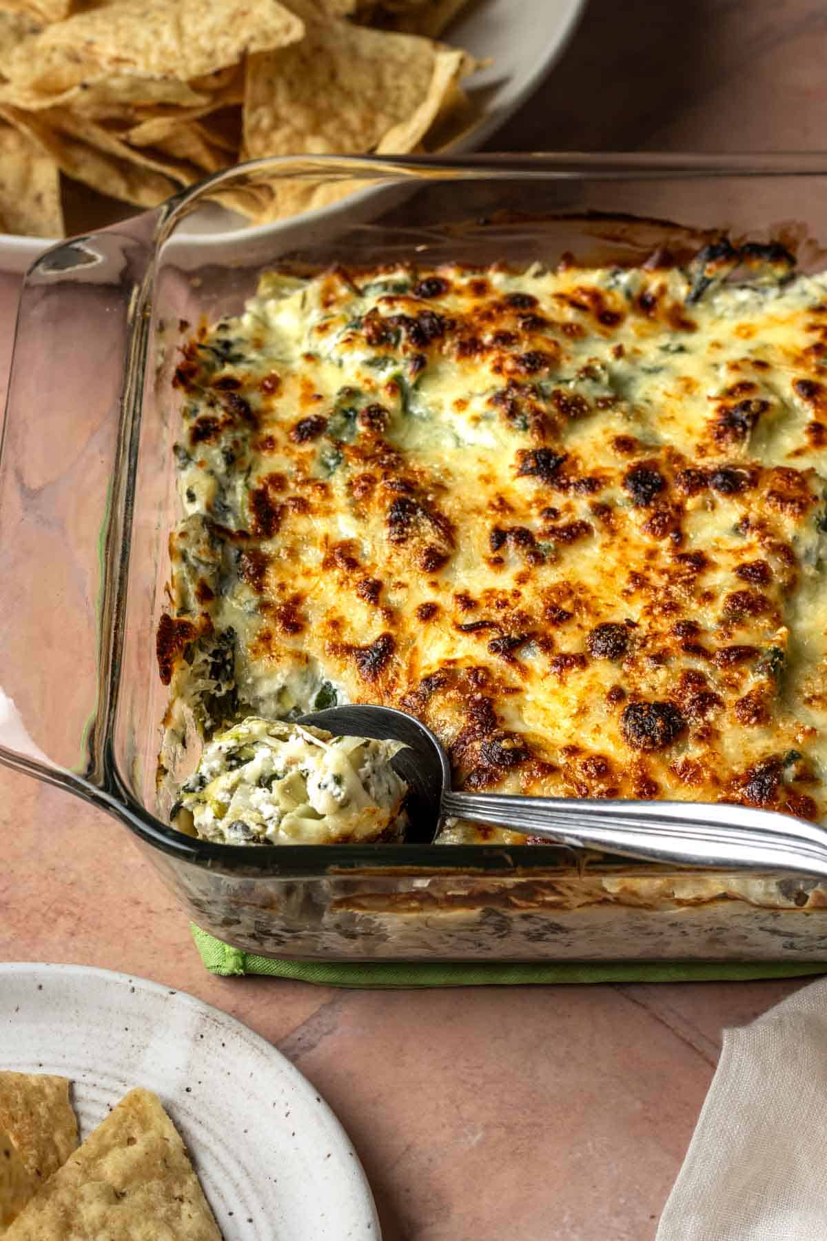 Baked spinach artichoke dip with a spoon scooping it out of the dish.
