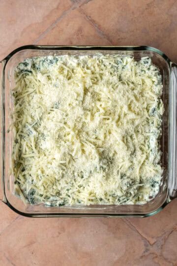 An 8x8 baking dish with spinach artichoke mixture topped with cheese.