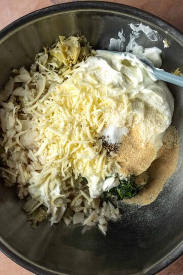 A large mixing bowl with greek yogurt and ingredients for spinach artichoke dip.