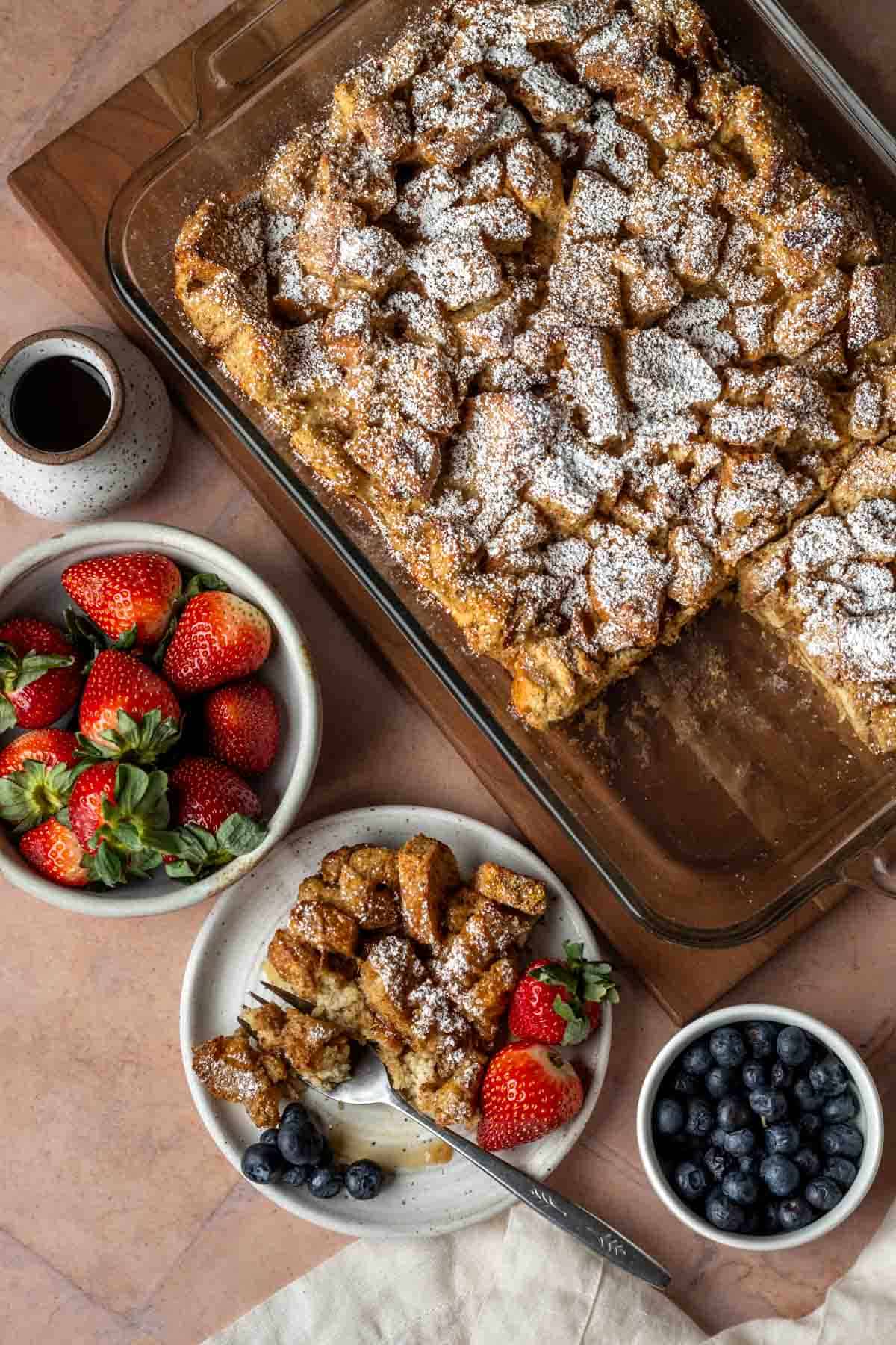 Overhead of sourdough French toast casserole with bowls of fresh berries.