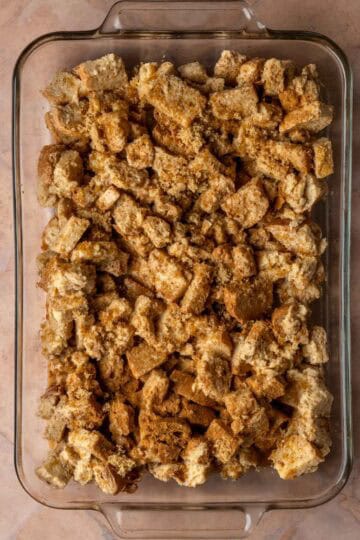 Cubes of egg-soaked bread in a baking dish topped with brown sugar.