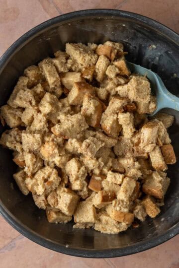 A mixing bowl of bread cubes tossed in an egg mixture.