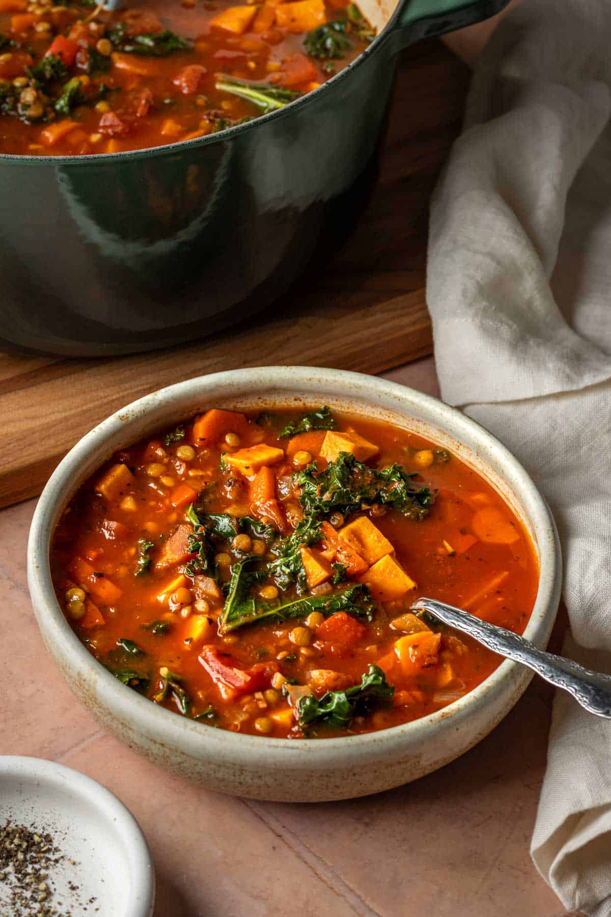 Vegetable lentil soup in a white bowl with a large pot in the background.