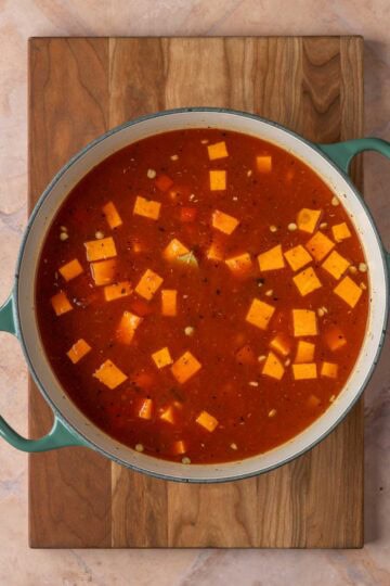 A pot of soup on a wooden cutting board.