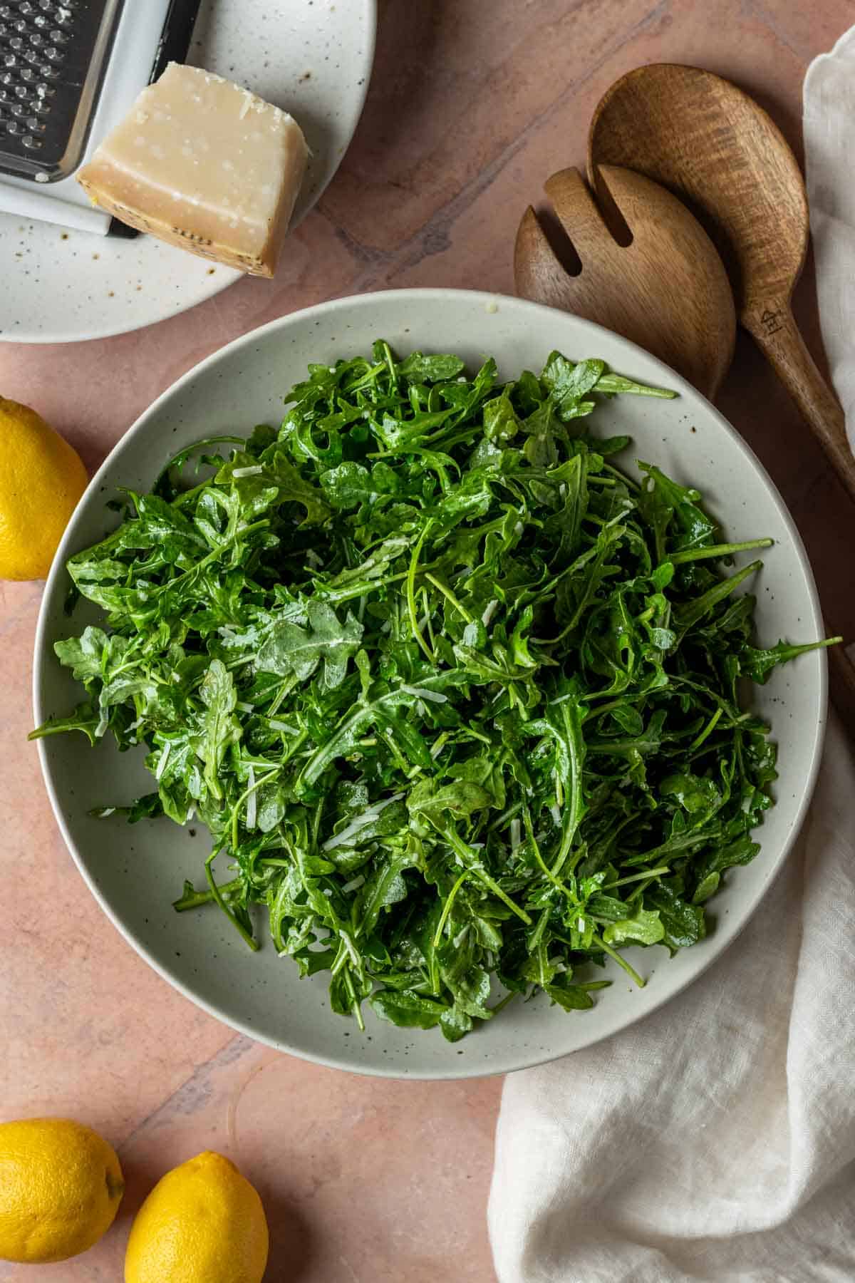 Arugula salad in a bowl with a block of parmesan cheese and lemons.